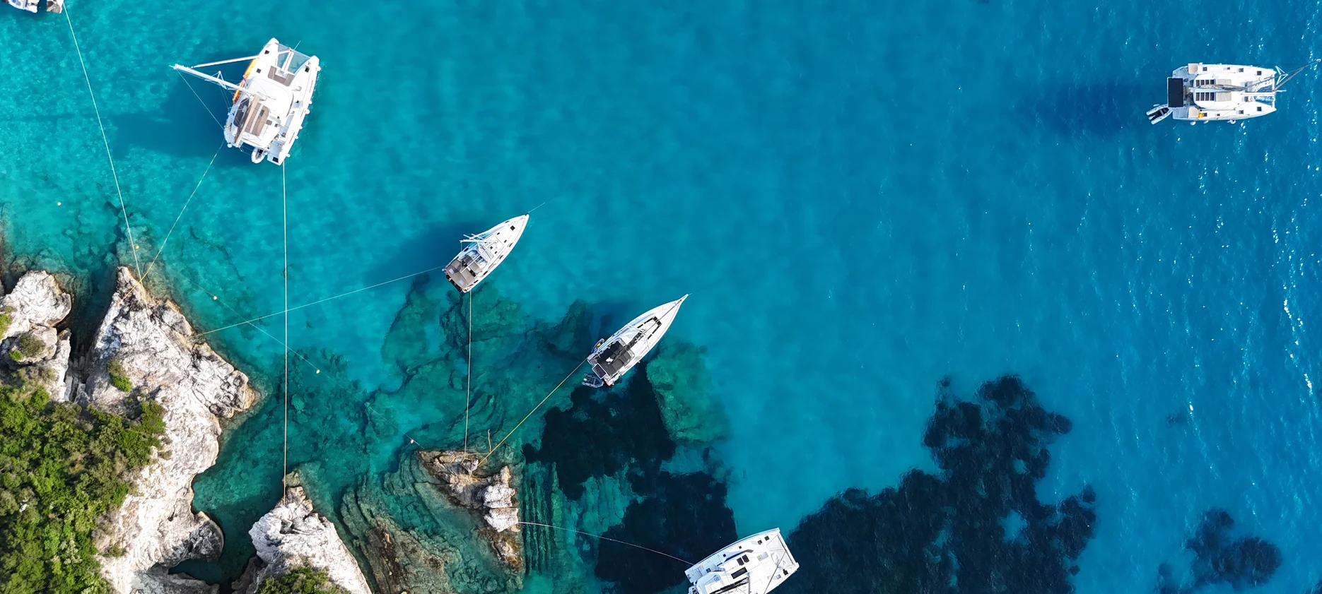 Aerial view of boats Med moored in a rocky Adriatic cove, each lying to a bow anchor with lines run back to the shore